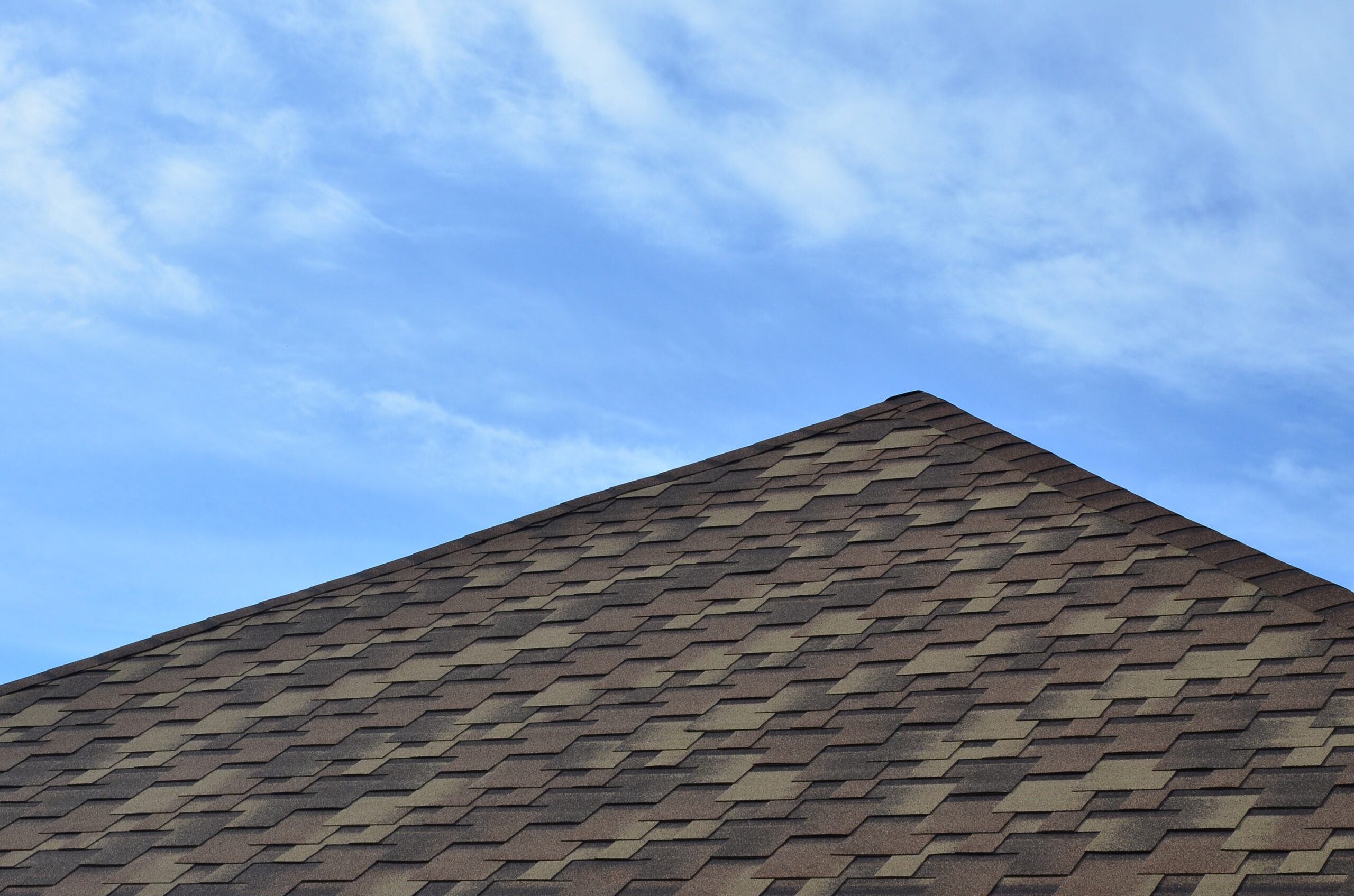 The roof of a residential house, covered with a modern flat bituminous waterproof coating under a blue cloudy sky. The concept of high-quality roofing with bituminous coating